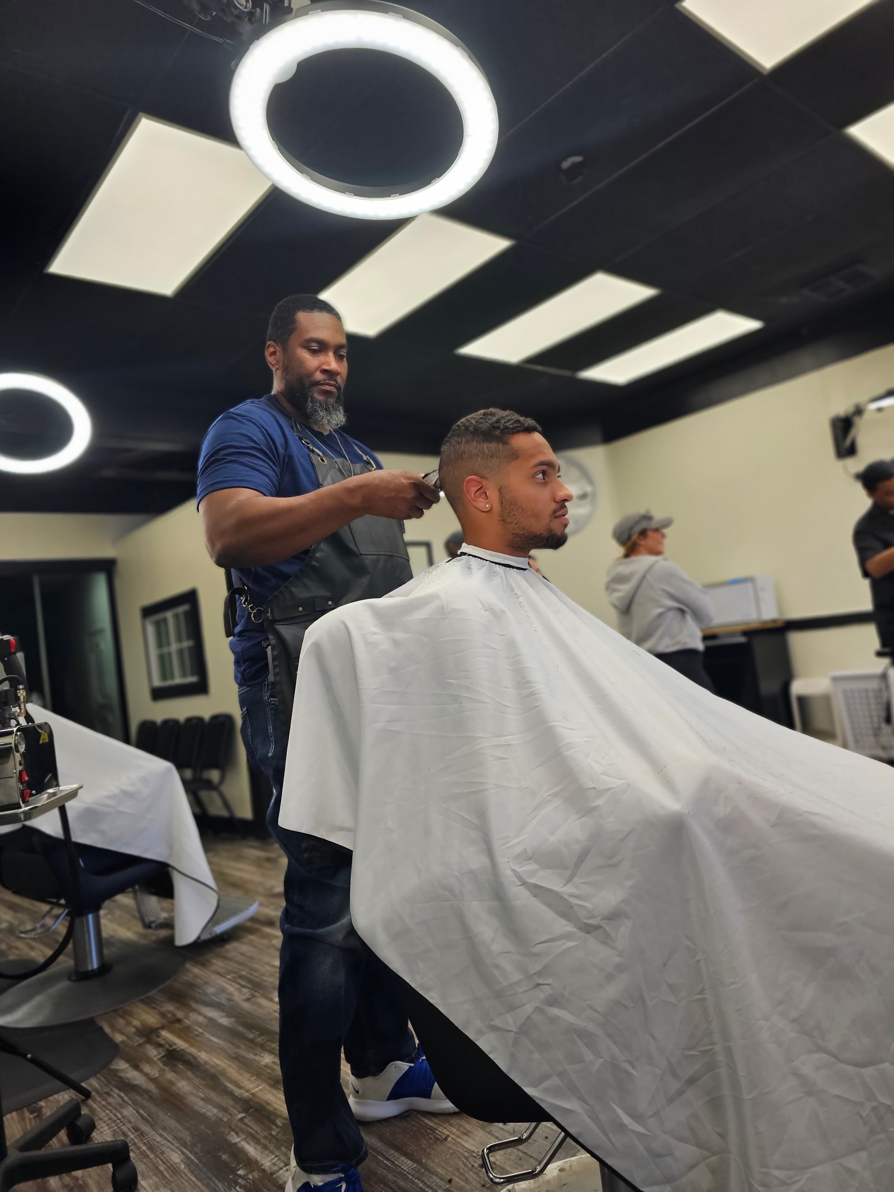 A barber trims a client's hair with clippers in a modern, well-lit barbershop.