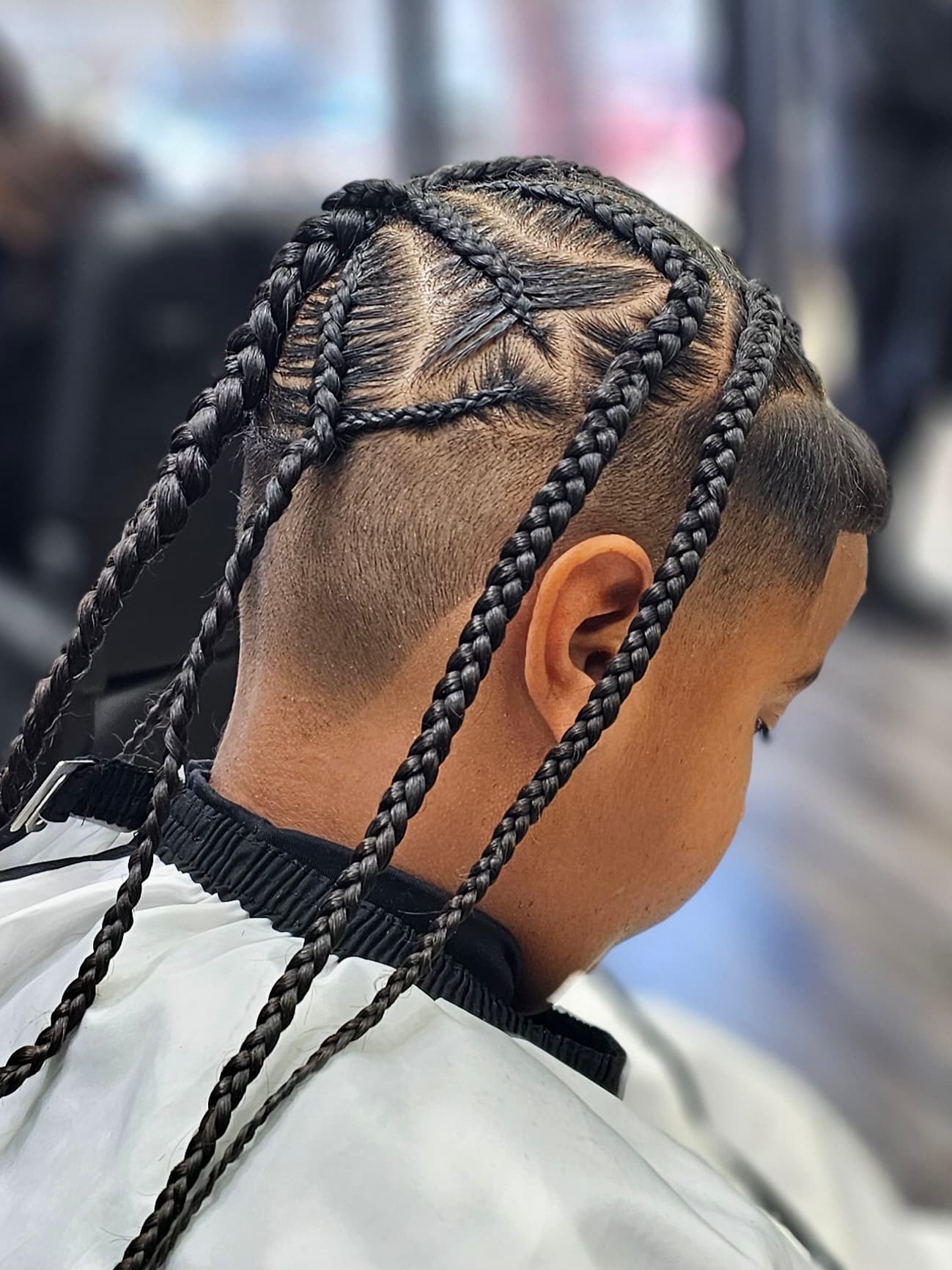 Intricate star-patterned braids and faded sides on a person in a white barber cape.
