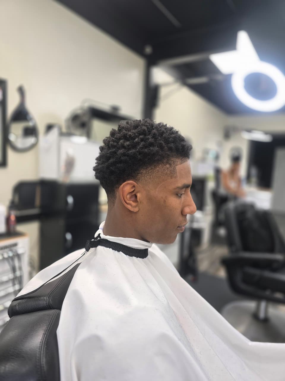 Profile of a man with a fresh taper fade and textured curls in a barbershop.