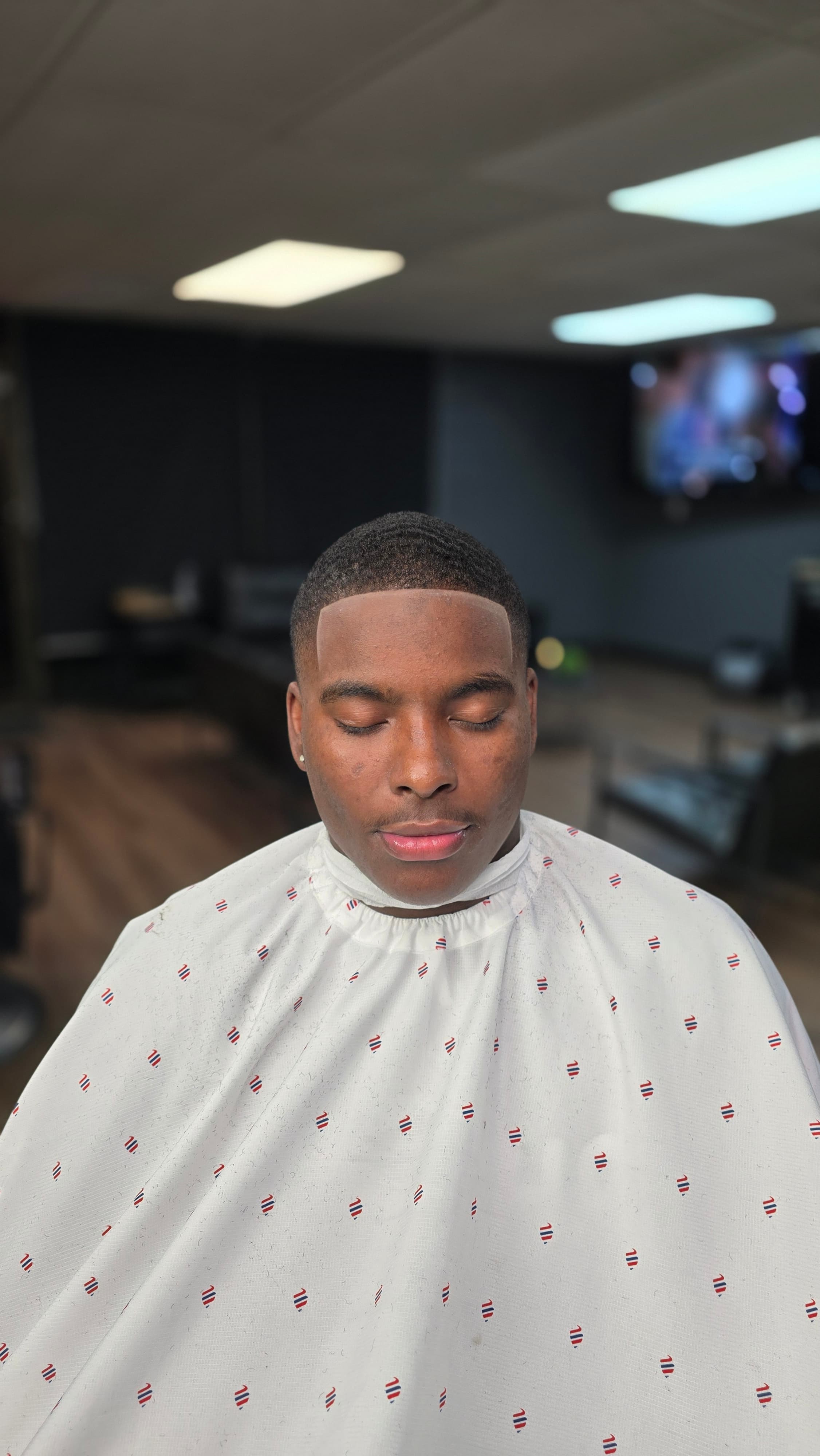 Young Black man with a fresh haircut and closed eyes wearing a white barber cape.