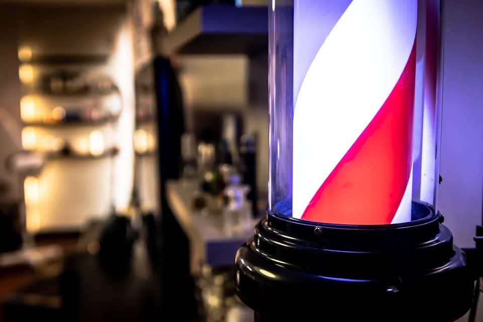 Close-up of a glowing red and white barber pole with a blurred barbershop background.