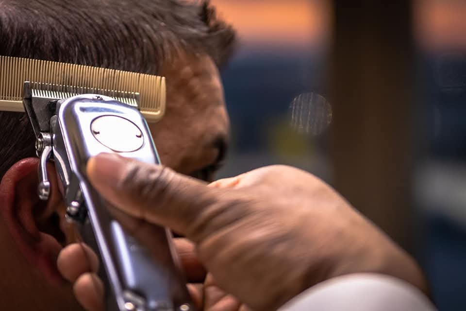 Barber's hand using silver electric clippers and a comb to trim a man's hair.