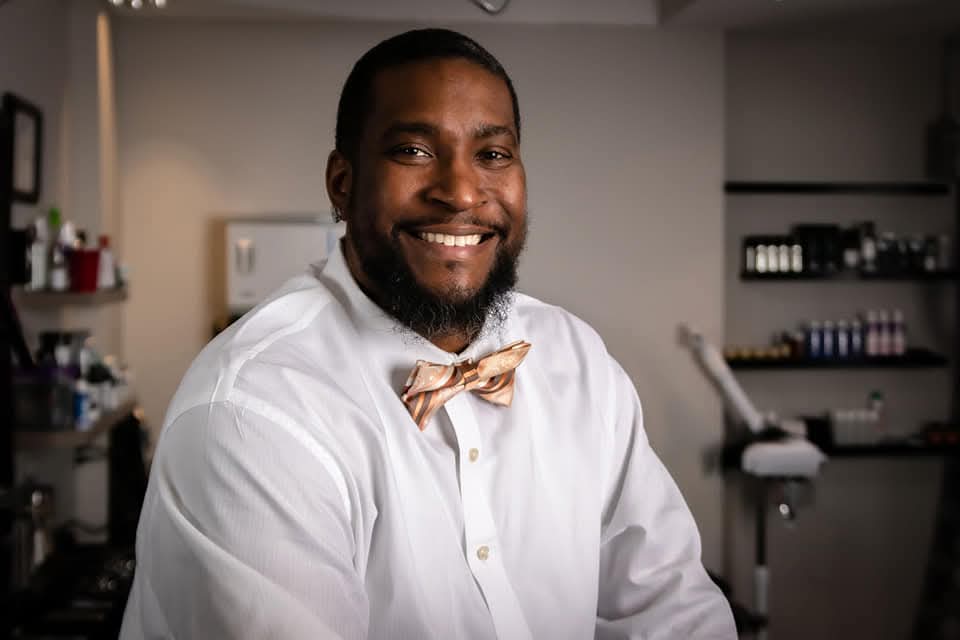 Smiling Black man with a beard wearing a white shirt and a patterned bow tie.