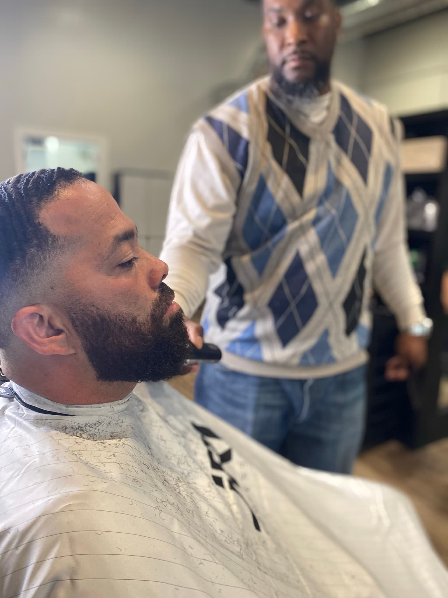 Professional barber using electric clippers to carefully trim and shape a client's full dark beard.