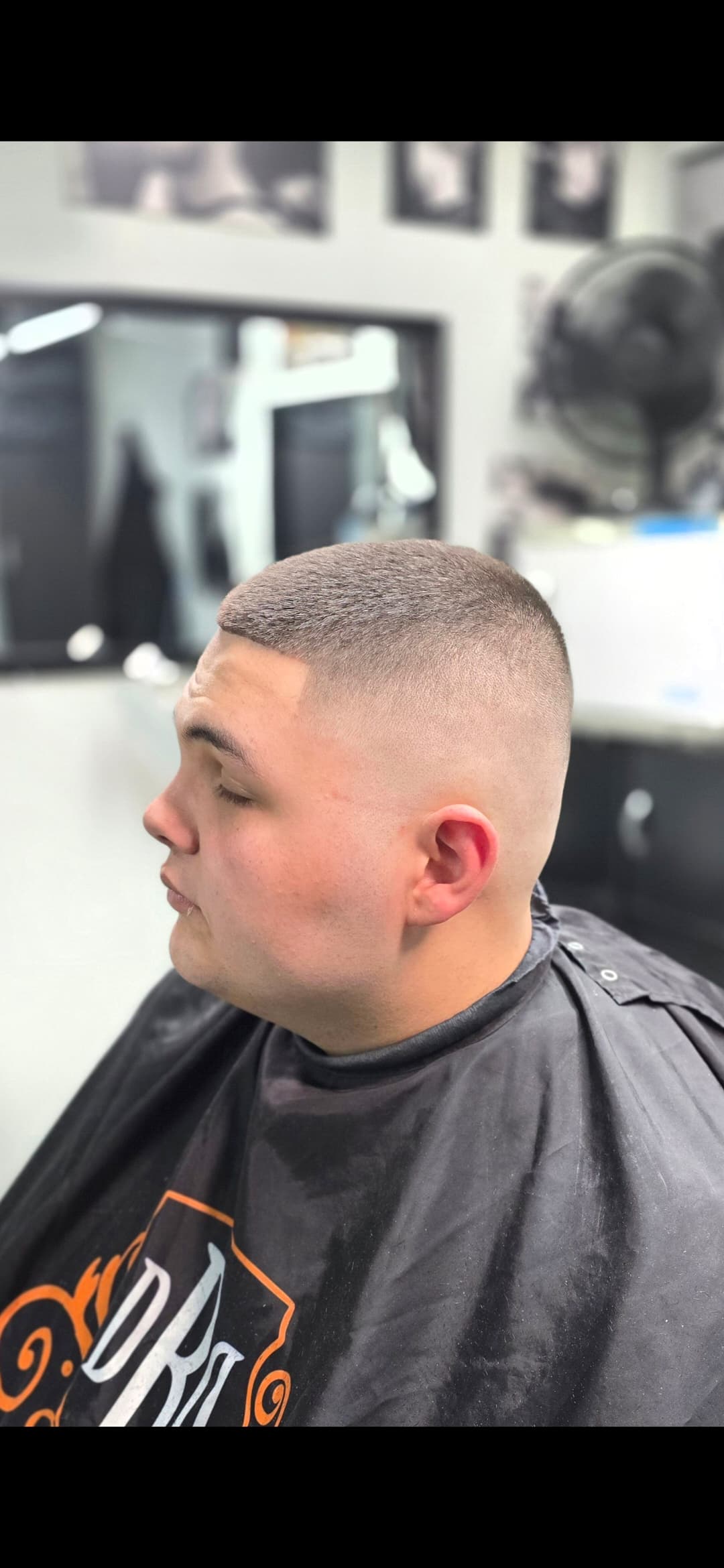 Man with a sharp high skin fade and buzz cut sitting in a barber chair.